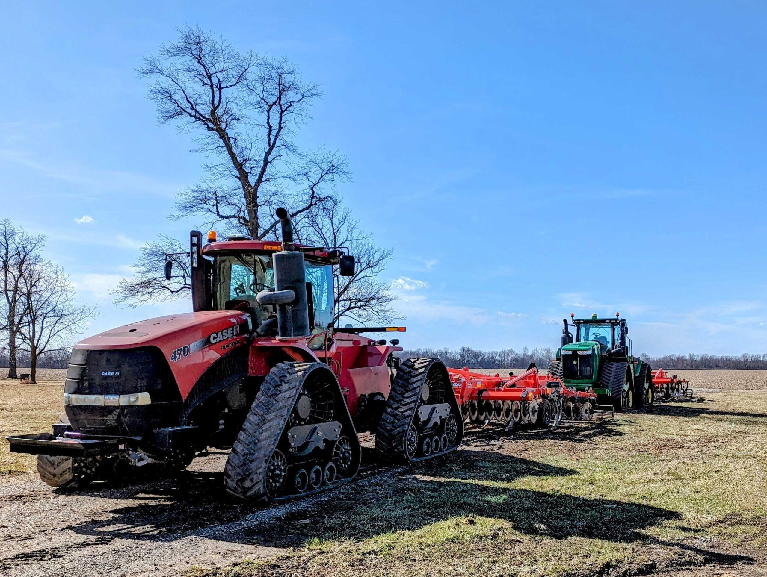 A red tractor and a green tractor with tillage equipment in a field