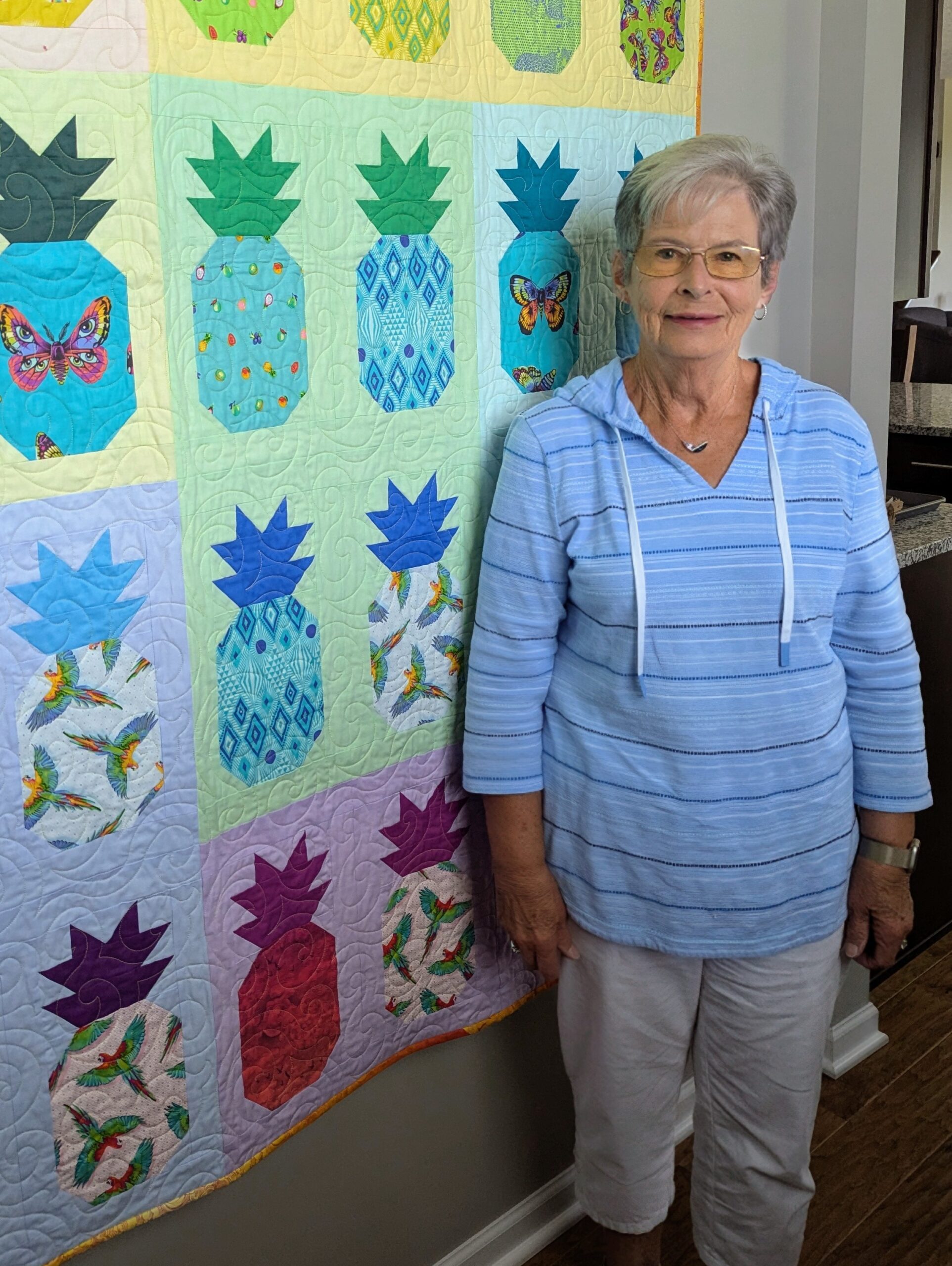 Madelyn Maupin standing beside one of her pineapple-pattern quilts