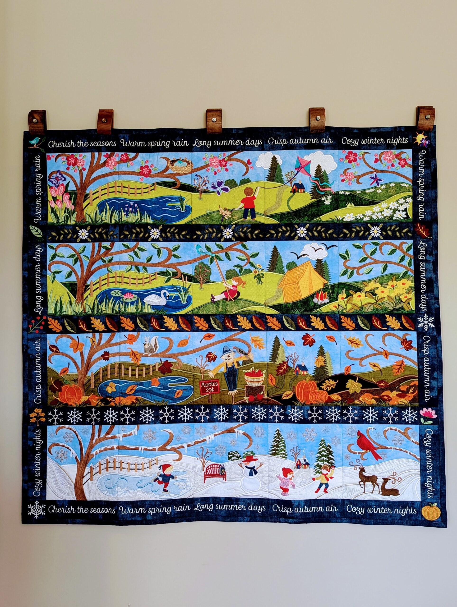 A hanging quilt showing scenes from all four seasons