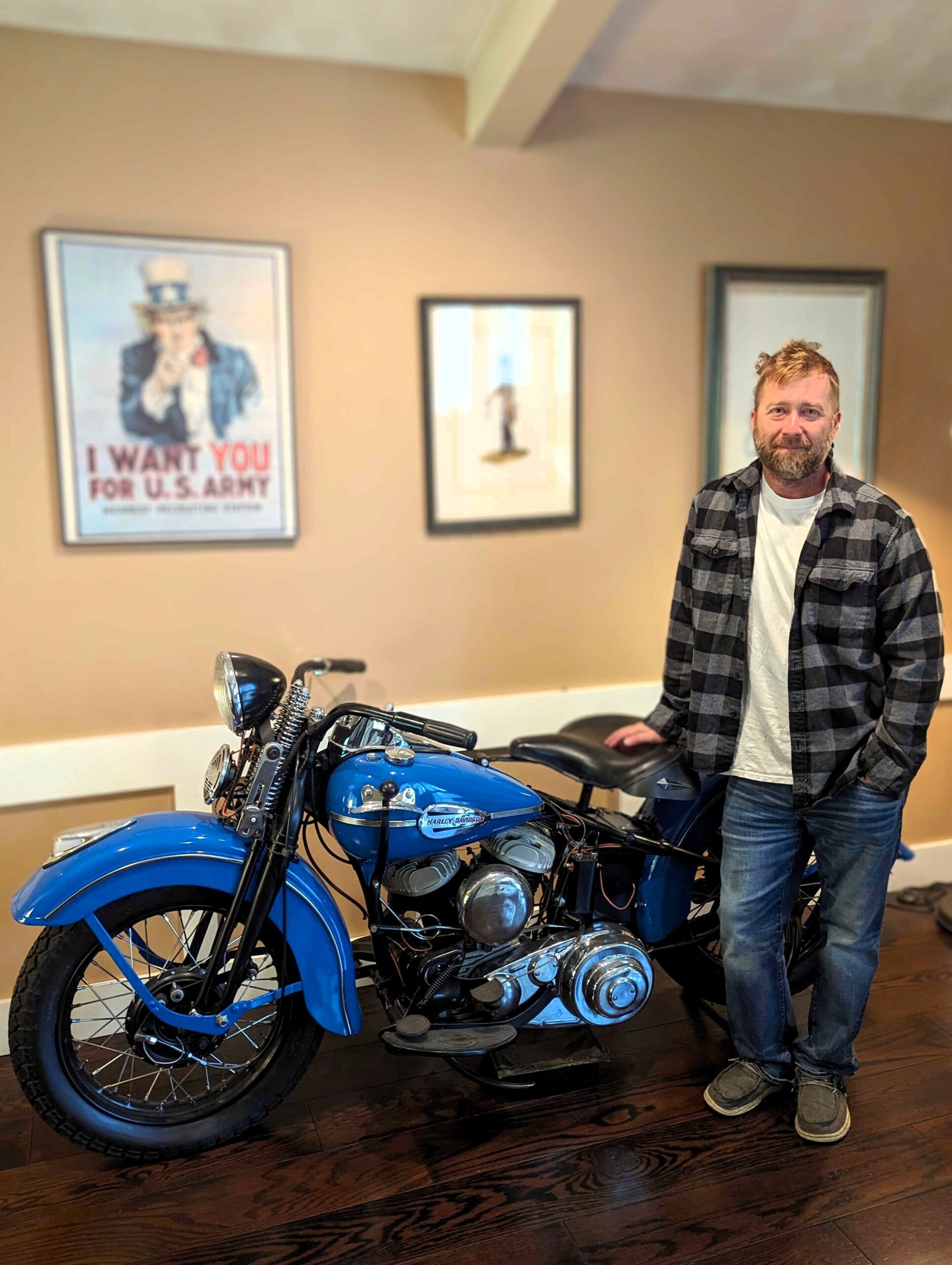 Eric Underwood standing beside his vintage blue Harley-Davidson in his living room